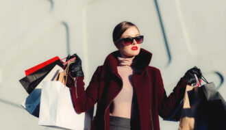 Office Style Diary - Stylish woman in burgundy coat and sunglasses carrying multiple shopping bags, fashion-forward shopper, luxury retail therapy, urban chic look with red lipstick