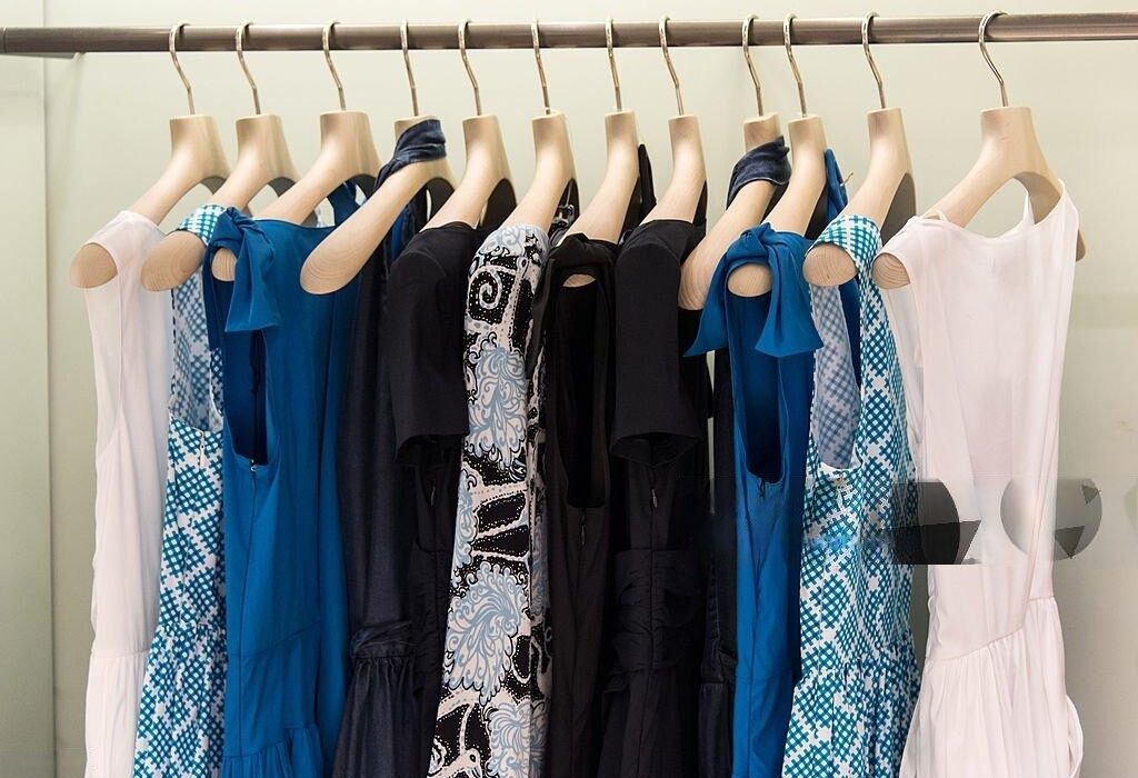 Office Style Diary- Rack of stylish blue, black, and white dresses with various patterns and solid colors on wooden hangers, showcasing elegant business casual fashion options.