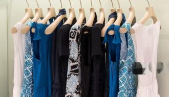 Office Style Diary- Rack of stylish blue, black, and white dresses with various patterns and solid colors on wooden hangers, showcasing elegant business casual fashion options.