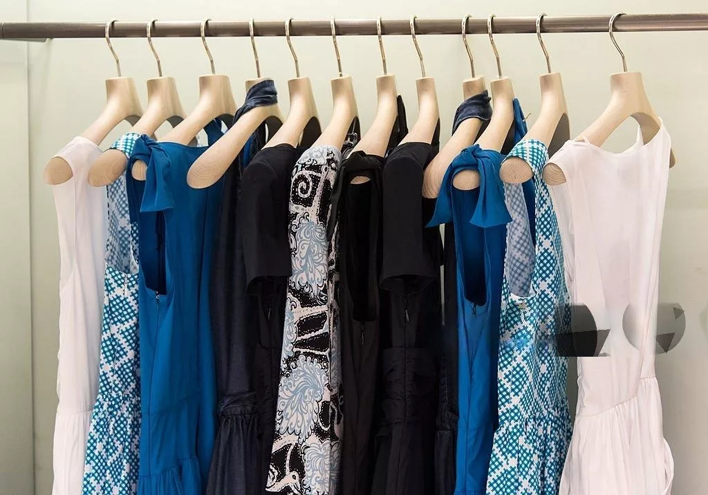 Office Style Diary- Rack of stylish blue, black, and white dresses with various patterns and solid colors on wooden hangers, showcasing elegant business casual fashion options.